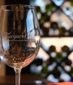 A wine glass on a table at Margaret Kuo's Kitchen with a premium wine selection in the background